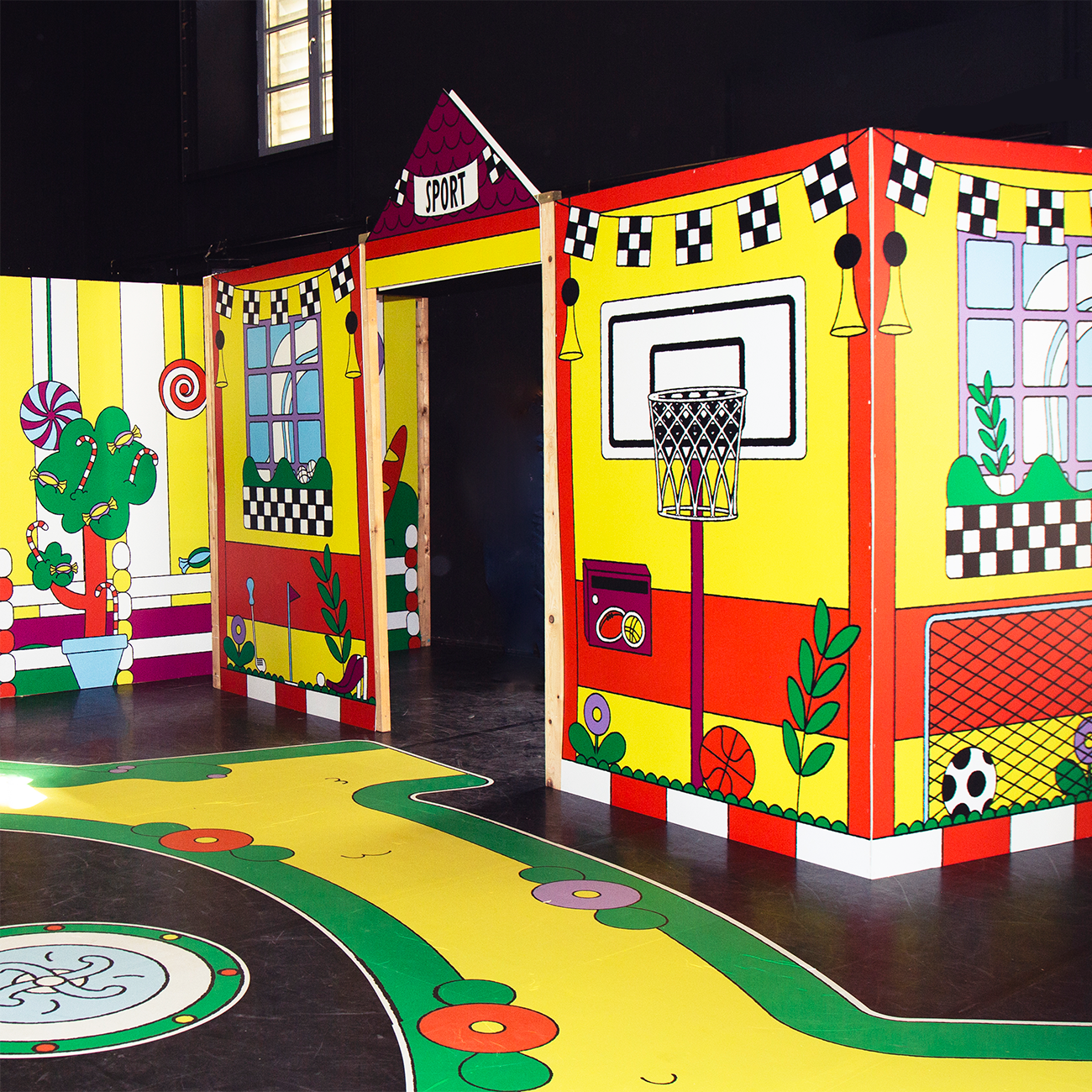 Colorful play area with cartoon-style sports theme, featuring a basketball hoop, checkerboard patterns, and vibrant murals on walls and floor.