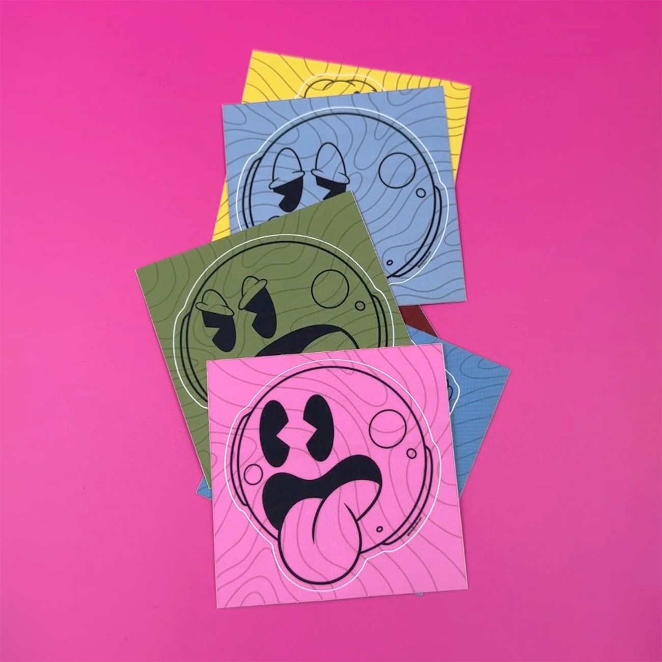 Kiss-cut sticker smiley faces in verschillende kleuren en gezichtsuitdrukkingen gedrukt op mat vinyl, tegen een roze achtergrond.