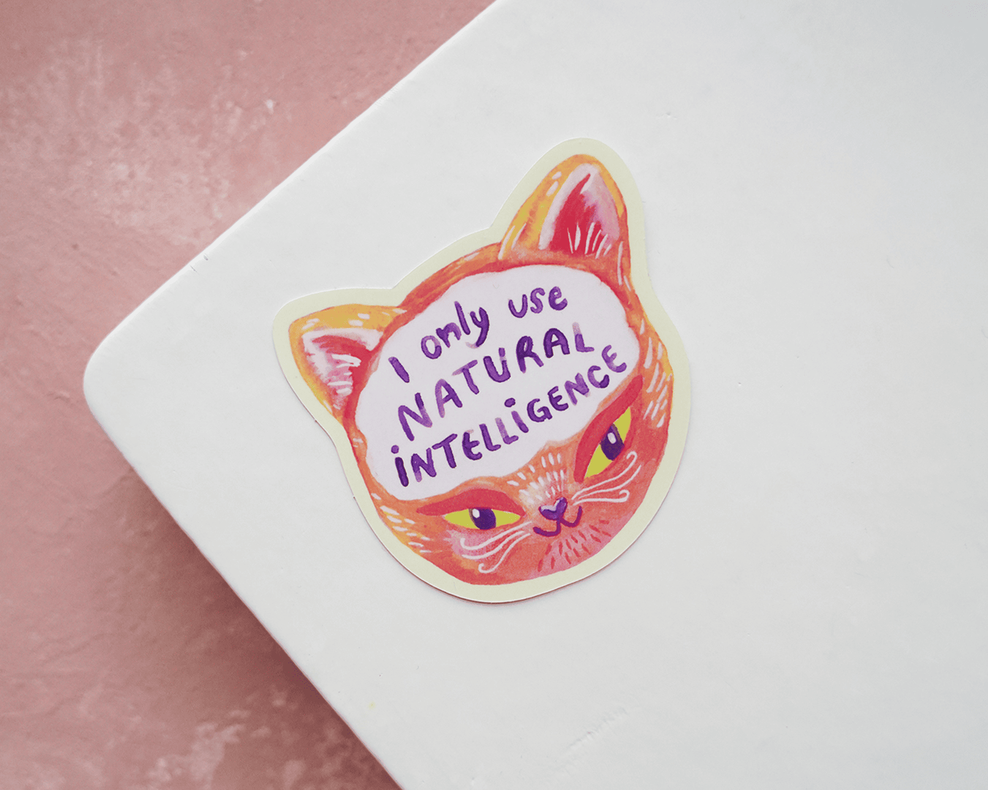 Contourgesneden kattenkopsticker met de tekst "I only use natural intelligence" op een wit notitieboek