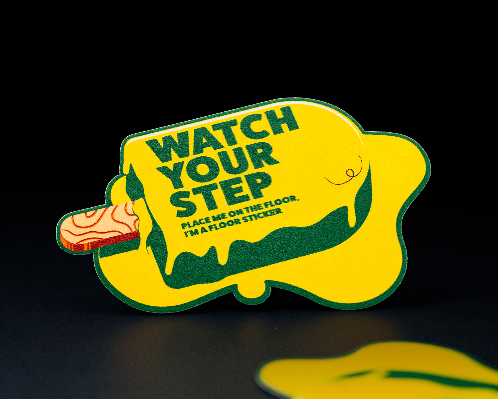 Yellow caution floor sticker shaped like a melting popsicle with "WATCH YOUR STEP" text in bold green letters.