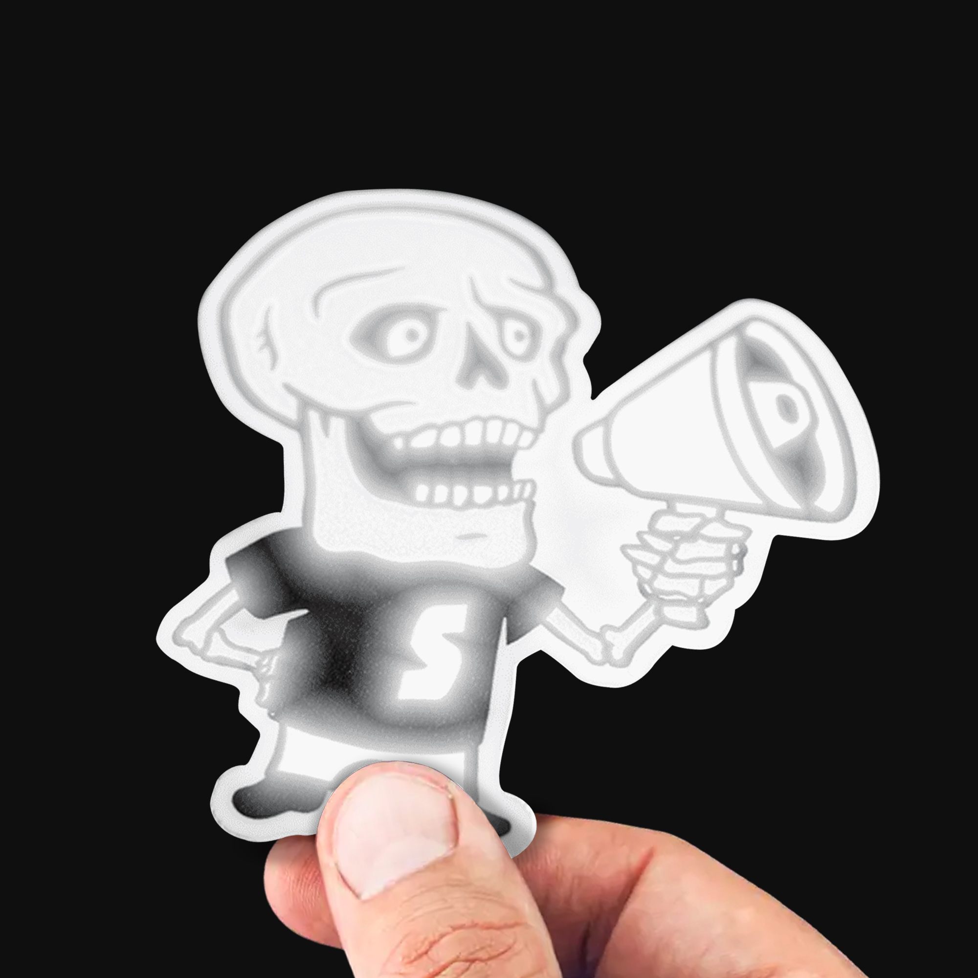 Hand met een reflecterende contourgesneden sticker van een skelet met een megafoon, die wit oplicht in direct licht