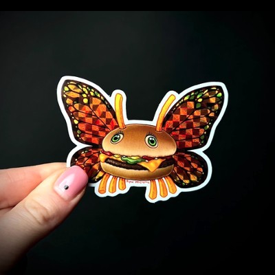 A hand holding up a prismatic sticker of a burger with a butterfly on it