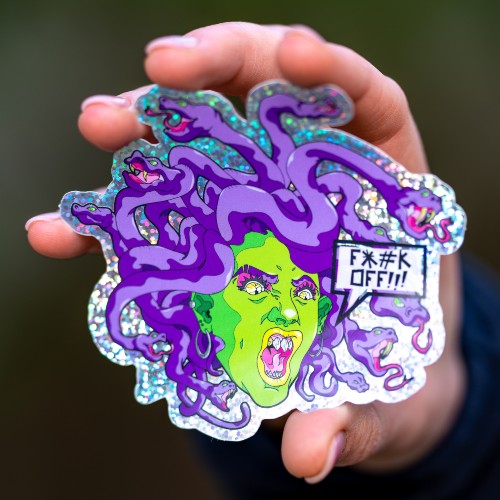 A person holding up a purple and green medusa sticker saying Fuck off